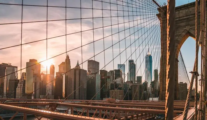 Manhattan skyline seen through the cables of the Brooklyn Bridge at sunset
