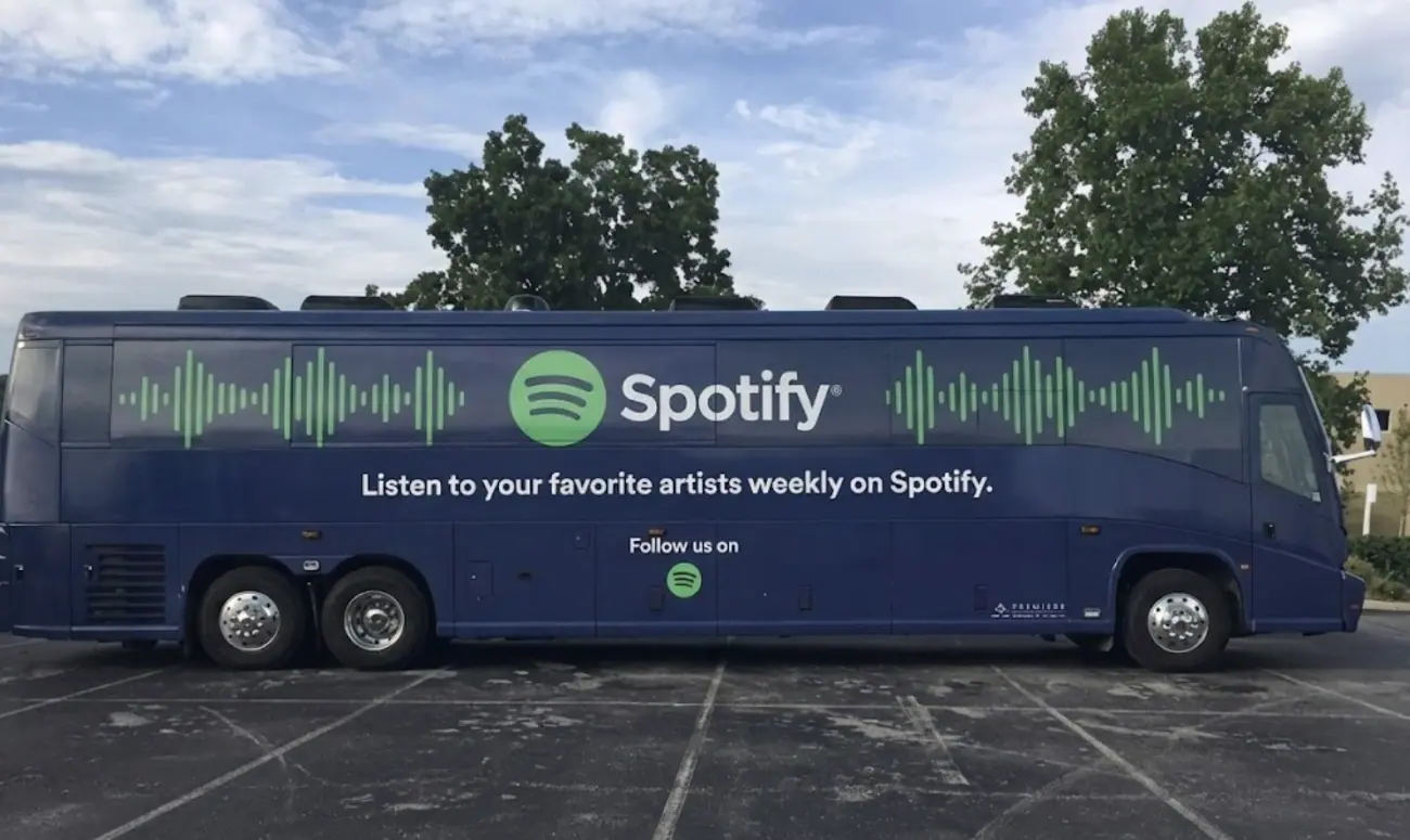 A large motorcoach featuring a full coach bus wrap for a Spotify brand takeover. This premium stadium & arena shuttle displays a sleek navy blue design with audio waveforms, illustrating a high-impact brand takeover for event shuttles. Designed for massive reach, these festival shuttle wraps provide experiential marketing directors a mobile billboard solution for national tours and large-scale marketing activations.
